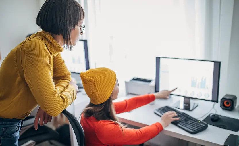 2 people with 1 person pointing at a monitor screen and the other person standing behind them.jpg